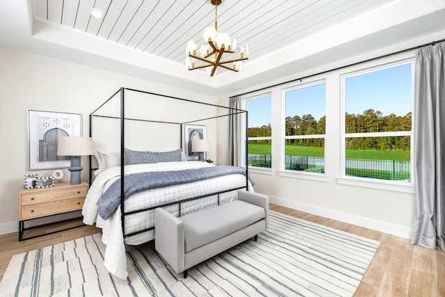 bedroom featuring a chandelier, light wood-type flooring, wood ceiling, and a tray ceiling