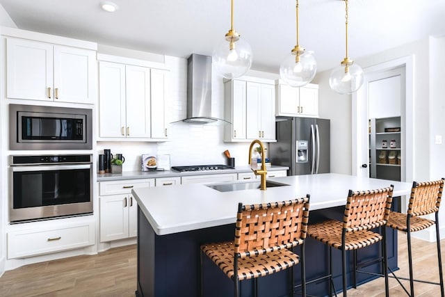 kitchen with a kitchen island with sink, sink, wall chimney exhaust hood, appliances with stainless steel finishes, and white cabinetry