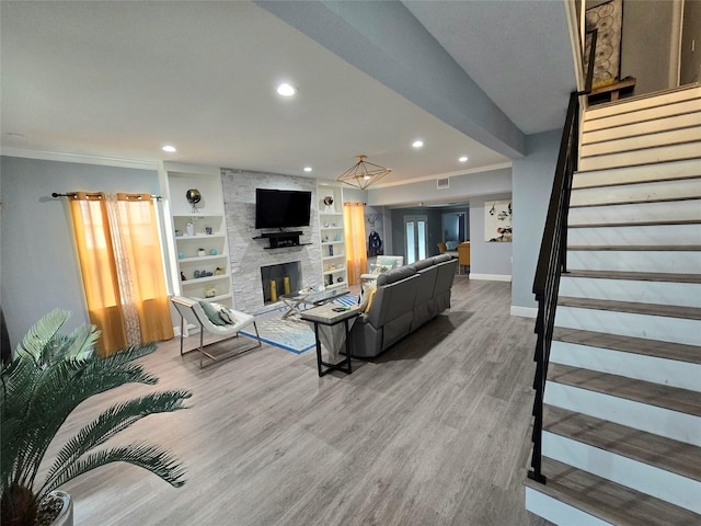 living room featuring a fireplace, crown molding, hardwood / wood-style floors, and built in features