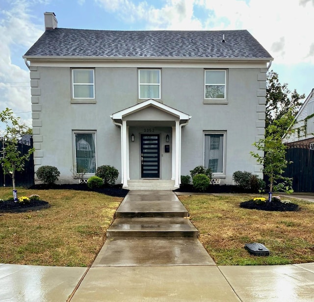 view of front of property featuring a front lawn, a chimney, a shingled roof, and stucco siding