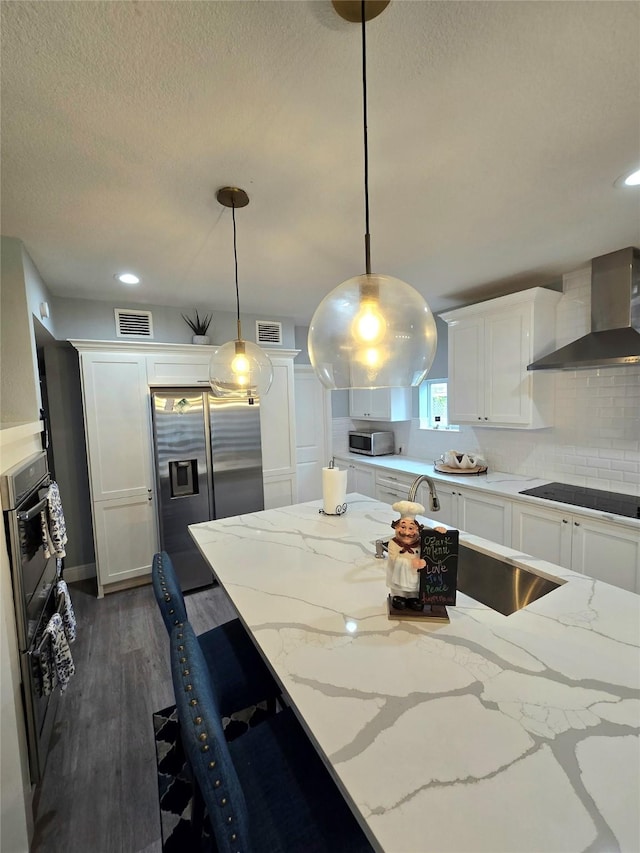 kitchen with black appliances, wall chimney exhaust hood, dark hardwood / wood-style floors, decorative light fixtures, and white cabinetry