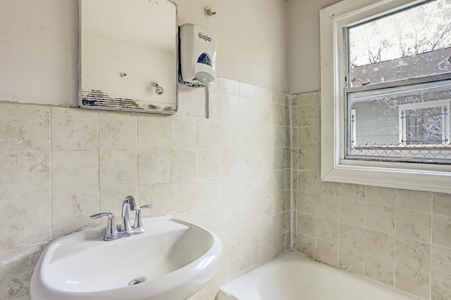 bathroom with water heater, sink, a bath, and tile walls