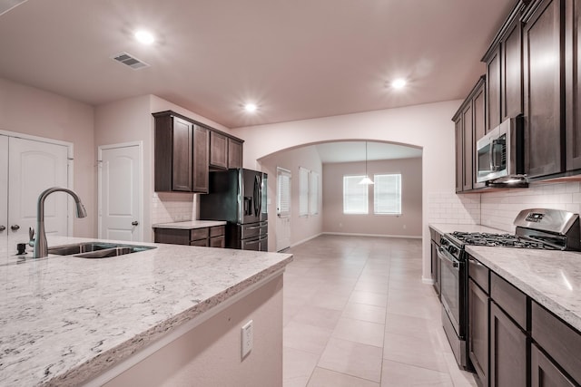 kitchen with light stone countertops, sink, stainless steel appliances, backsplash, and dark brown cabinets