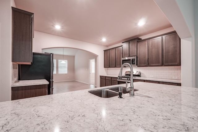 kitchen with dark brown cabinets, light stone counters, sink, and appliances with stainless steel finishes