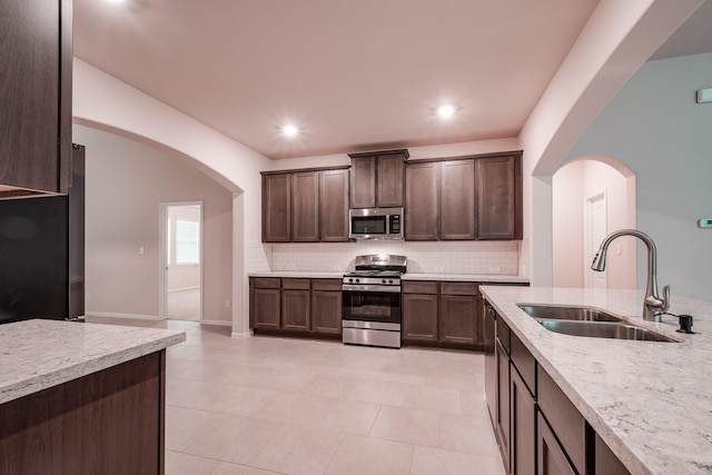 kitchen with backsplash, sink, light stone countertops, appliances with stainless steel finishes, and dark brown cabinets