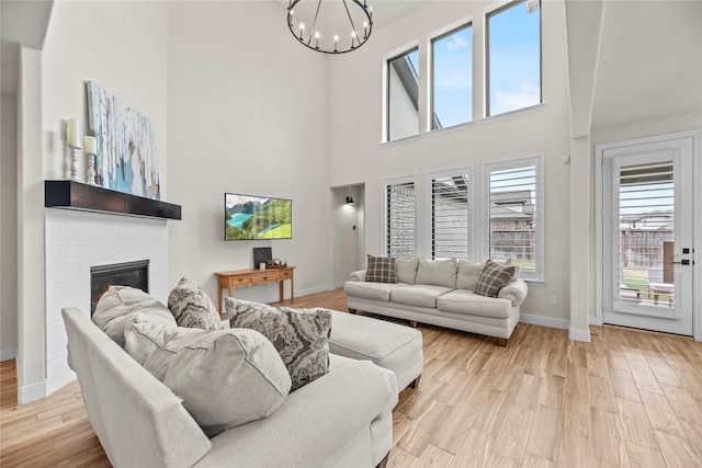 living room featuring a large fireplace, light wood-type flooring, a towering ceiling, and an inviting chandelier