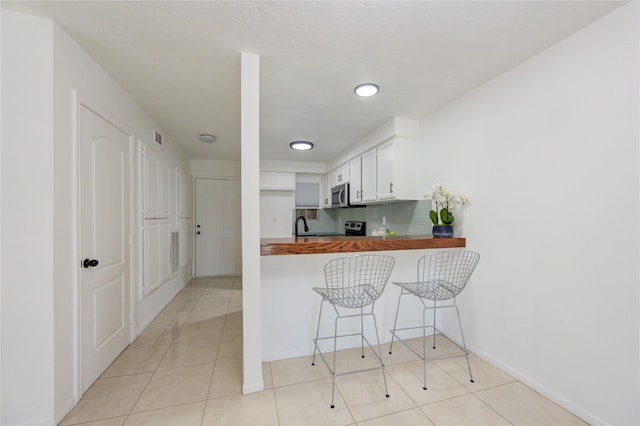 kitchen with kitchen peninsula, decorative backsplash, butcher block countertops, a breakfast bar area, and light tile patterned flooring