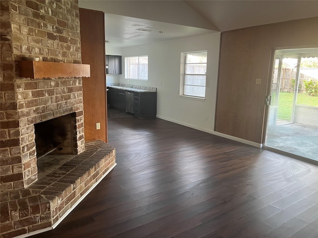 unfurnished living room featuring dark wood-type flooring, a healthy amount of sunlight, and a brick fireplace