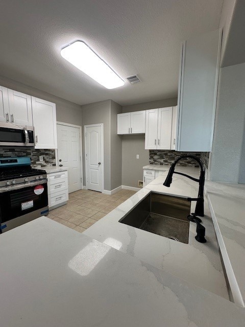 kitchen with white cabinetry, sink, tasteful backsplash, a textured ceiling, and appliances with stainless steel finishes