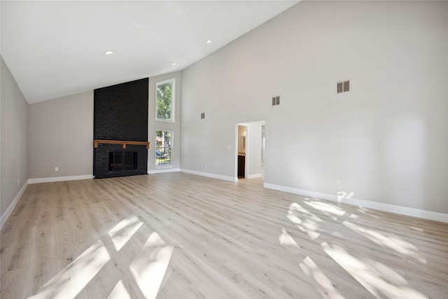 unfurnished living room featuring a fireplace, high vaulted ceiling, and light hardwood / wood-style floors