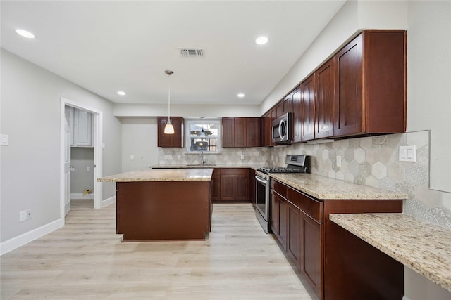 kitchen featuring appliances with stainless steel finishes, tasteful backsplash, light stone counters, decorative light fixtures, and light hardwood / wood-style floors