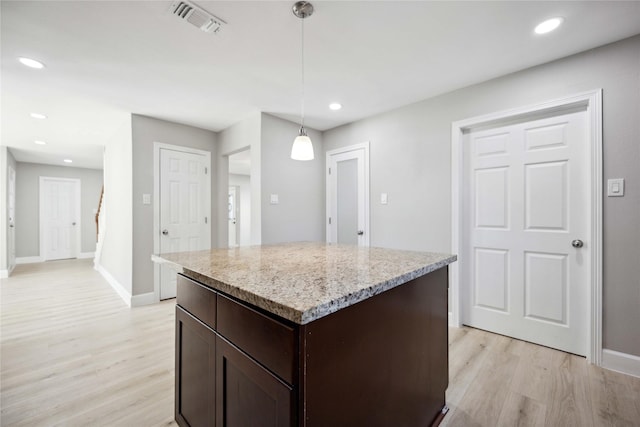 kitchen with pendant lighting, light hardwood / wood-style flooring, a kitchen island, light stone counters, and dark brown cabinetry