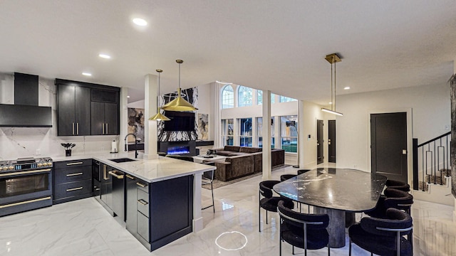 kitchen featuring sink, wall chimney exhaust hood, hanging light fixtures, stainless steel range oven, and kitchen peninsula