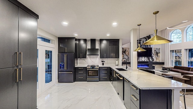 kitchen with appliances with stainless steel finishes, a kitchen breakfast bar, sink, wall chimney range hood, and hanging light fixtures