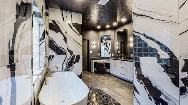 bathroom with a bath, vanity, tile patterned floors, and tile walls