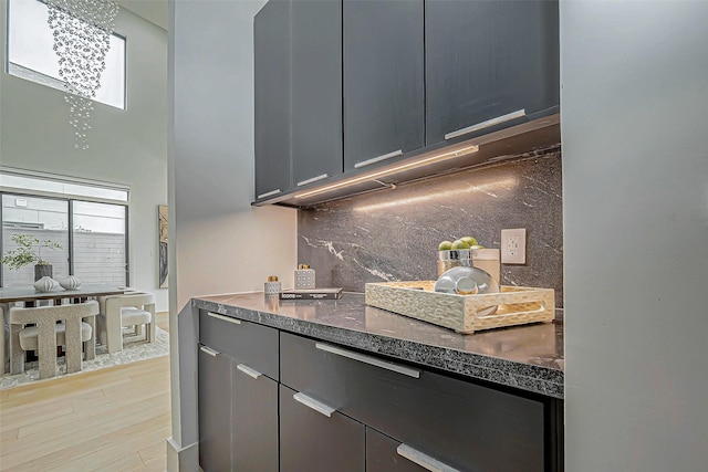 kitchen with light hardwood / wood-style floors, dark stone countertops, backsplash, and an inviting chandelier