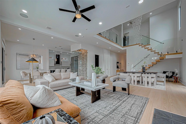 living room with ceiling fan, a towering ceiling, and light wood-type flooring