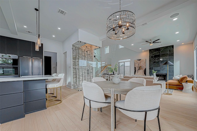 dining room with a tiled fireplace, light hardwood / wood-style flooring, a towering ceiling, and ceiling fan with notable chandelier