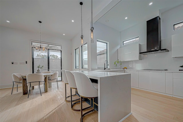 kitchen featuring wall chimney exhaust hood, pendant lighting, light hardwood / wood-style flooring, white cabinets, and a kitchen island