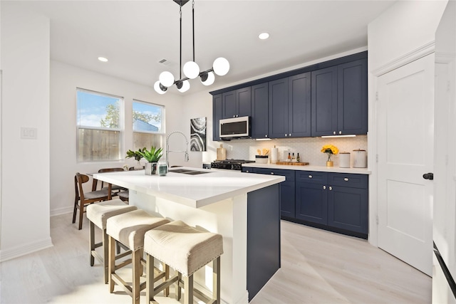 kitchen with light wood-type flooring, sink, hanging light fixtures, and an island with sink