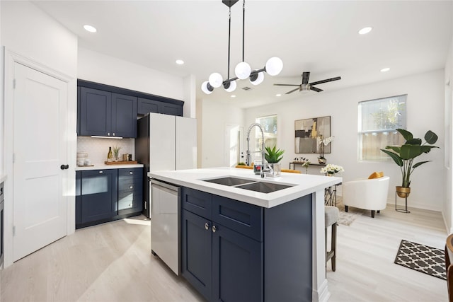 kitchen featuring stainless steel dishwasher, blue cabinets, a kitchen island with sink, and sink