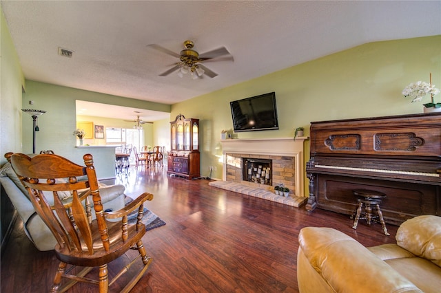 living room featuring a brick fireplace, a textured ceiling, vaulted ceiling, ceiling fan, and hardwood / wood-style floors