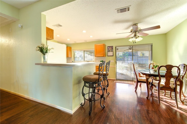 kitchen with kitchen peninsula, a kitchen breakfast bar, a textured ceiling, ceiling fan, and dark wood-type flooring