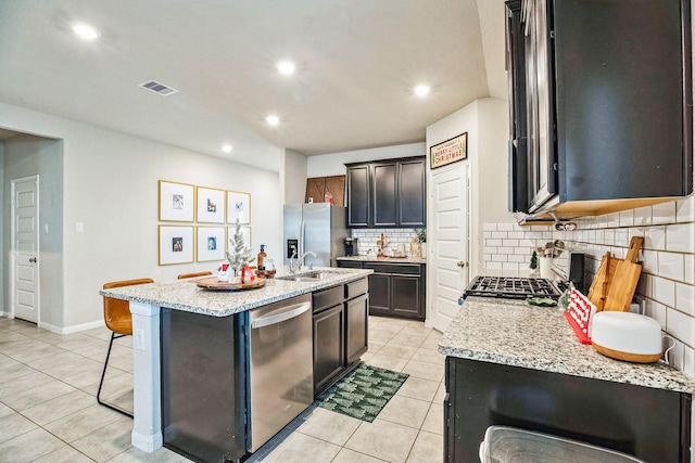 kitchen featuring a kitchen bar, light stone countertops, stainless steel appliances, a center island with sink, and light tile patterned flooring