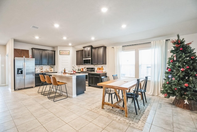 kitchen featuring a breakfast bar, backsplash, a center island with sink, appliances with stainless steel finishes, and dark brown cabinets