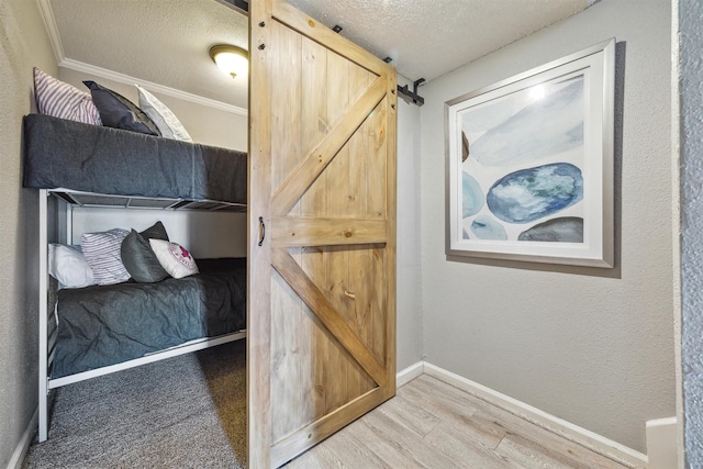 bedroom with a barn door, light hardwood / wood-style floors, a textured ceiling, and ornamental molding