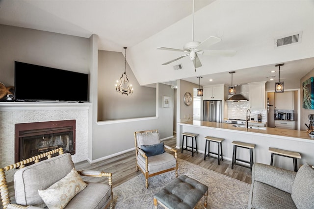 living room with hardwood / wood-style floors, ceiling fan with notable chandelier, sink, and vaulted ceiling