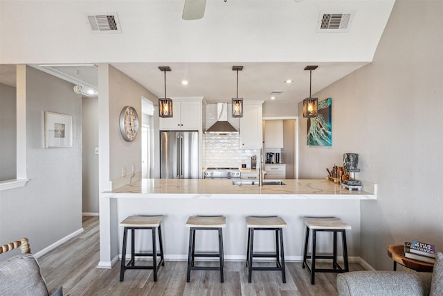 kitchen with wall chimney exhaust hood, a kitchen breakfast bar, high end refrigerator, kitchen peninsula, and white cabinets