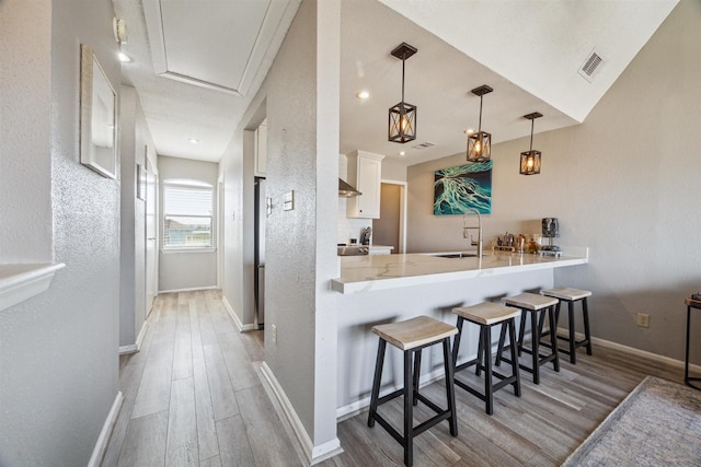 kitchen featuring a kitchen bar, kitchen peninsula, light wood-type flooring, sink, and pendant lighting