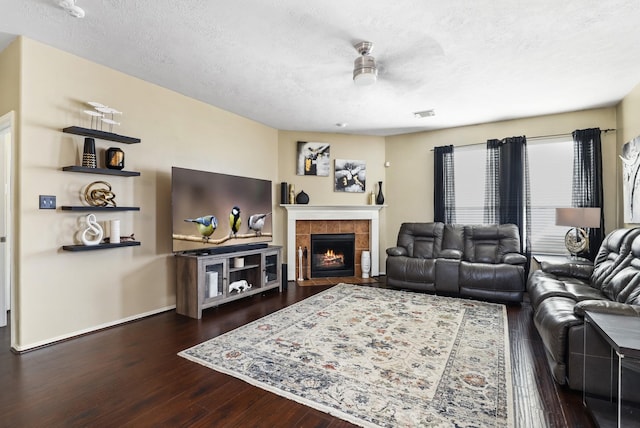 living room with a textured ceiling, a tile fireplace, ceiling fan, and dark hardwood / wood-style floors