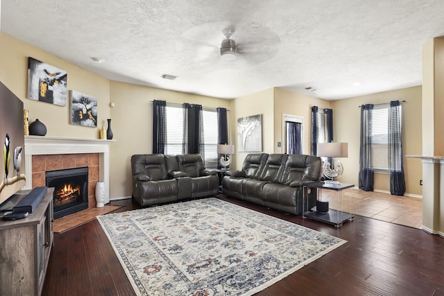 living room featuring a fireplace, a textured ceiling, ceiling fan, and dark wood-type flooring