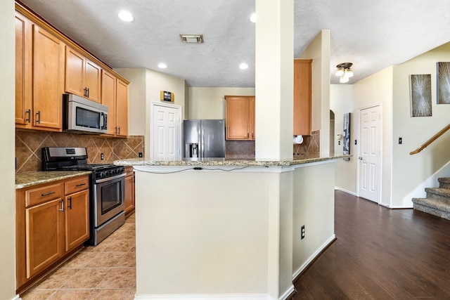 kitchen featuring light stone countertops, kitchen peninsula, a textured ceiling, stainless steel appliances, and light hardwood / wood-style flooring