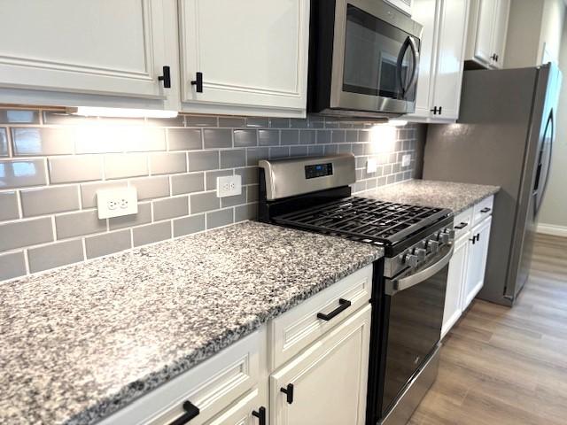 kitchen with decorative backsplash, light stone counters, stainless steel appliances, light hardwood / wood-style floors, and white cabinetry