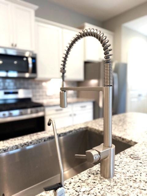 details featuring light stone countertops, stainless steel appliances, white cabinetry, and tasteful backsplash