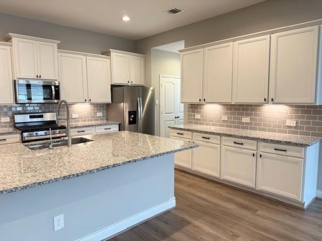 kitchen featuring light stone countertops, hardwood / wood-style floors, white cabinets, and appliances with stainless steel finishes