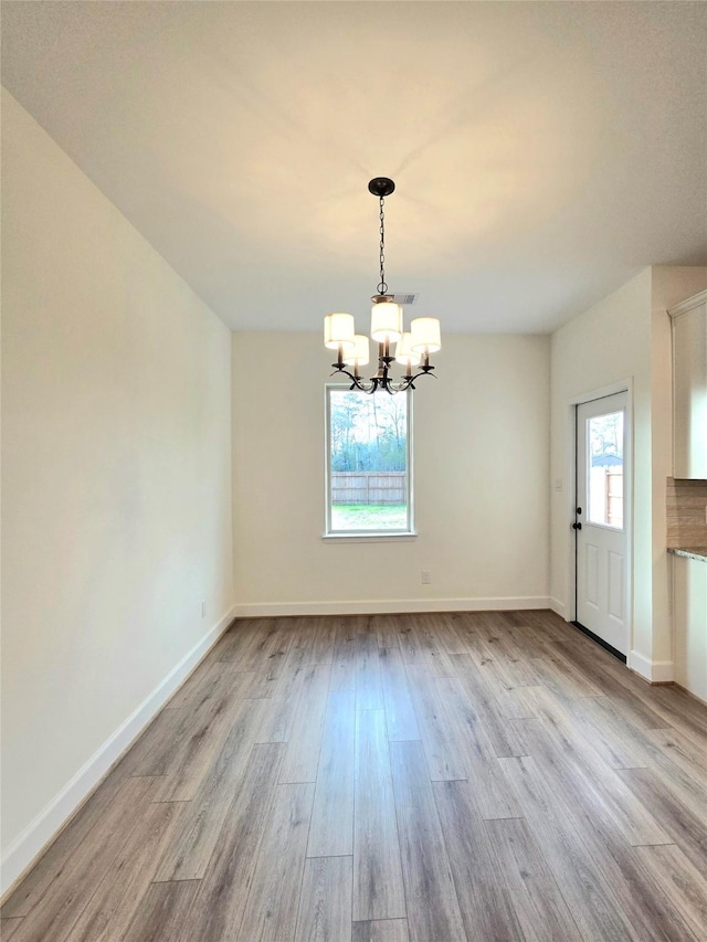 unfurnished dining area featuring light wood-type flooring and a notable chandelier