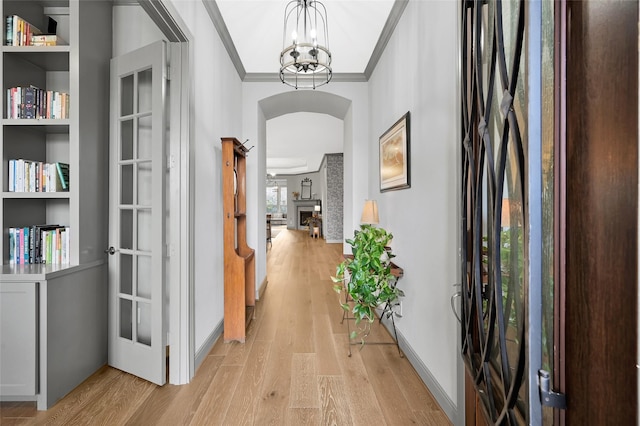 corridor with a notable chandelier, light wood-type flooring, and crown molding