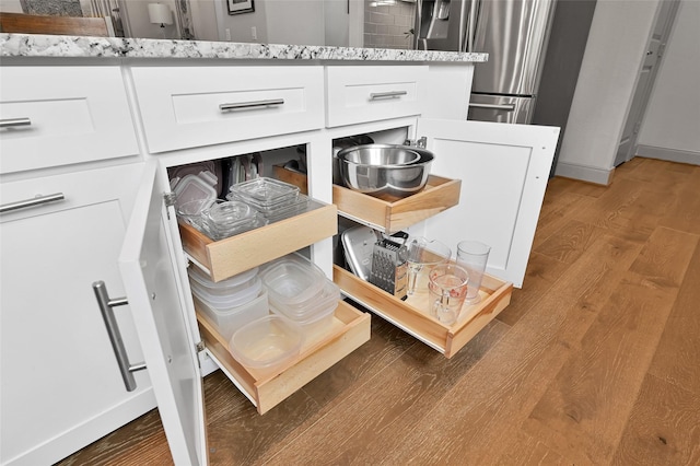 interior details featuring white cabinets, stainless steel fridge, light stone countertops, and wood-type flooring