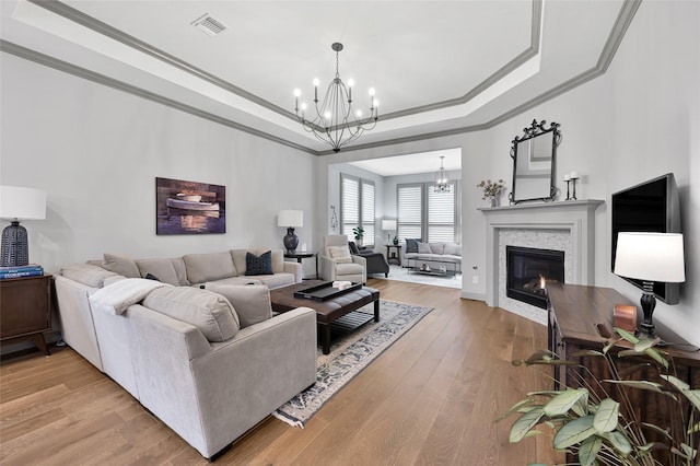 living room featuring a tray ceiling, an inviting chandelier, ornamental molding, and hardwood / wood-style flooring