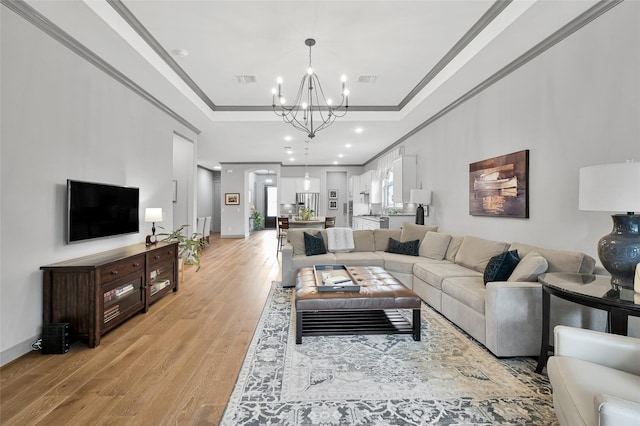 living room featuring light hardwood / wood-style floors, a raised ceiling, ornamental molding, and an inviting chandelier