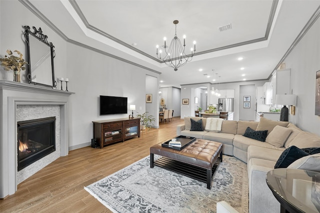 living room featuring a raised ceiling, light hardwood / wood-style flooring, ornamental molding, and a notable chandelier