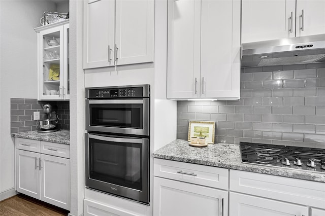 kitchen with backsplash, gas stovetop, light stone countertops, stainless steel double oven, and white cabinetry