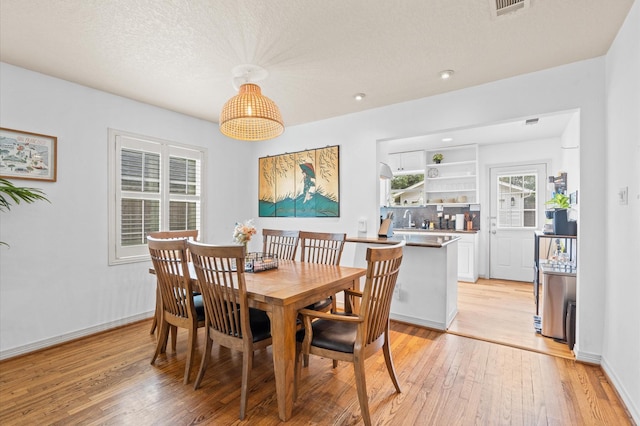 dining area with a textured ceiling, light wood-type flooring, and sink