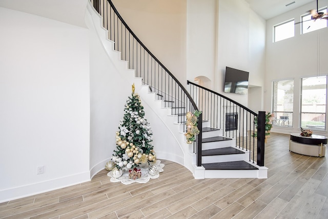 stairs with plenty of natural light, a towering ceiling, and hardwood / wood-style floors