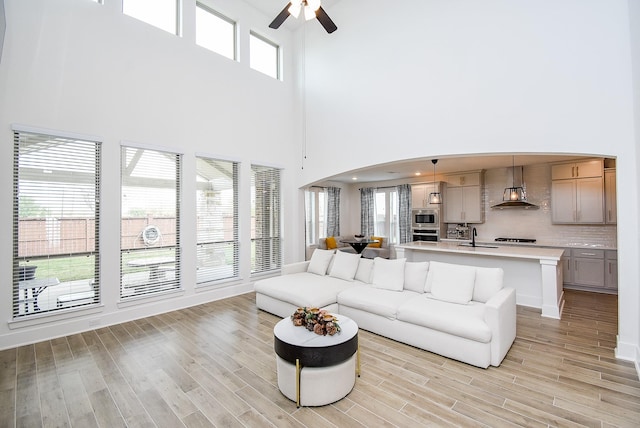 living room featuring ceiling fan, sink, a towering ceiling, and light hardwood / wood-style floors