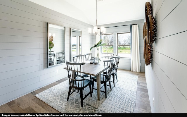 dining room featuring hardwood / wood-style flooring, wood walls, and an inviting chandelier